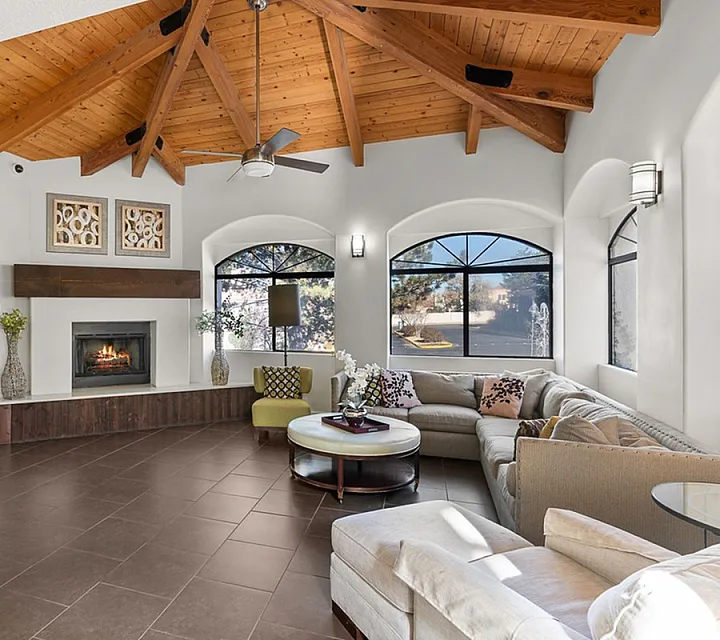Inviting living room with a vaulted wood ceiling, elegant fireplace, and large windows, perfect for relaxation and gatherings at Pavilions Apartments in Albuquerque