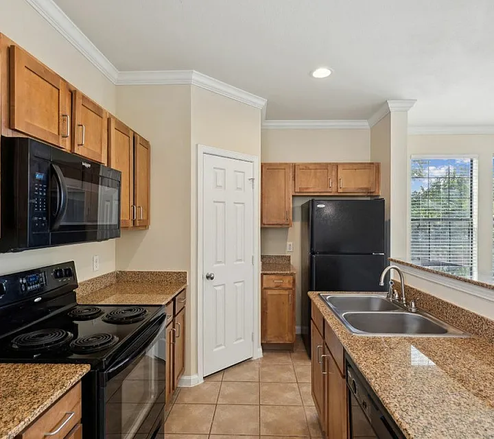 Modern kitchen design showcasing granite countertops, sleek black appliances, and abundant natural light through large windows at Enclave at Golden Triangle in Fort Worth TX