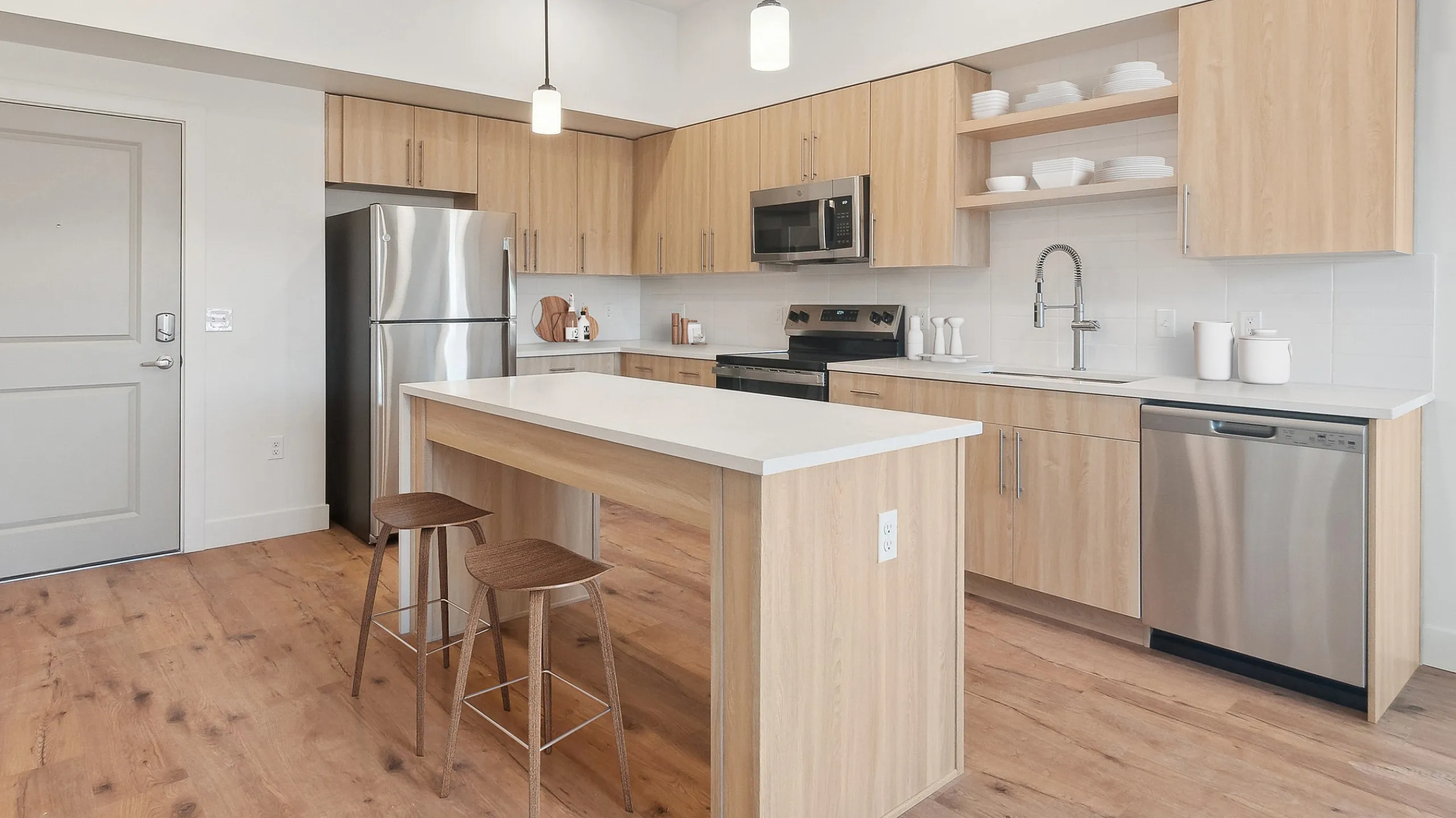 Showing a 2-bedroom apartment with a modern kitchen at Current Apartments in Murray, UT with sleek wood cabinets, stainless steel appliances, and island seating in a bright open-concept space.