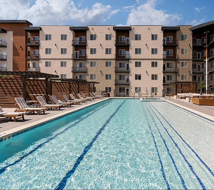 Elegant apartment complex featuring a pristine outdoor swimming pool with relaxing lounge chairs under wooden pergolas.