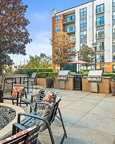 Chic outdoor patio with cozy seating, modern grills, and lush trees beside a stylish apartment complex, perfect for relaxation and entertaining at Cottonwood Westside Apartments in West Midtown Atlanta