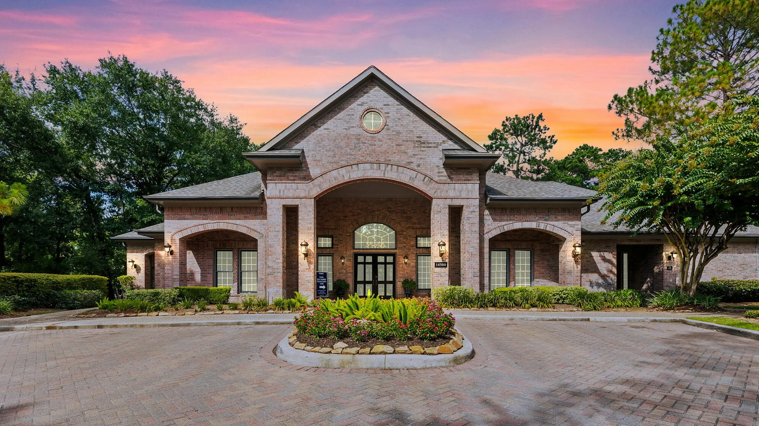 Elegant brick building with lush landscaping and welcoming entrance, set against a stunning sunset backdrop.