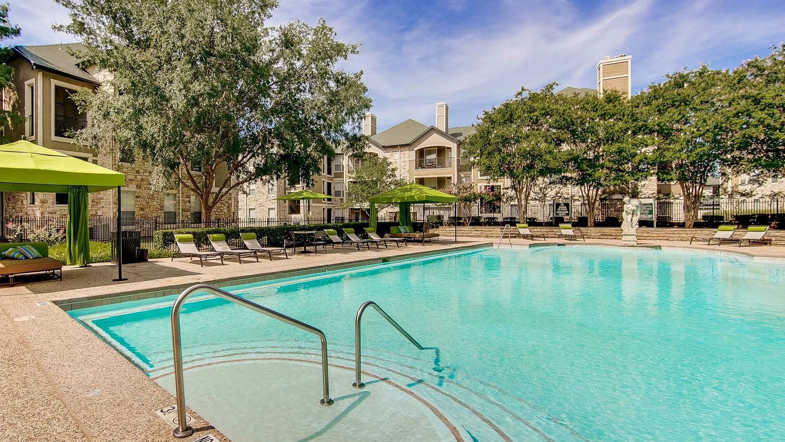 Luxurious poolside view at a modern apartment complex, featuring tranquil waters, green cabanas, and lush landscaping under a bright blue sky at Stonebriar at Frisco Apartments