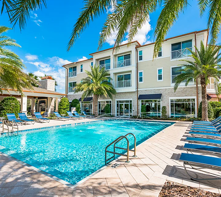 Luxurious apartment complex featuring a sparkling swimming pool surrounded by palm trees and comfortable lounge chairs for a perfect relaxation haven at The Marq at Highland Park in Westchase Tampa