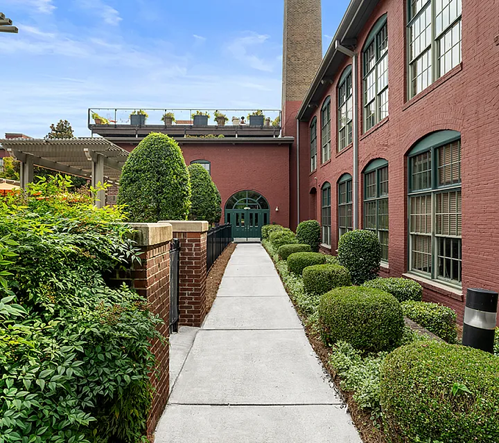 Charming brick apartment complex with lush landscaped pathway and modern windows at Alpha Mill apartments in Charlotte NC