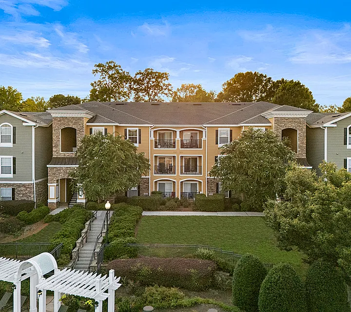 Charming apartment complex with elegant architecture, lush greenery, and inviting pathways under a clear blue sky at Cottonwood Reserve Apartments in Steele Creek Charlotte NC