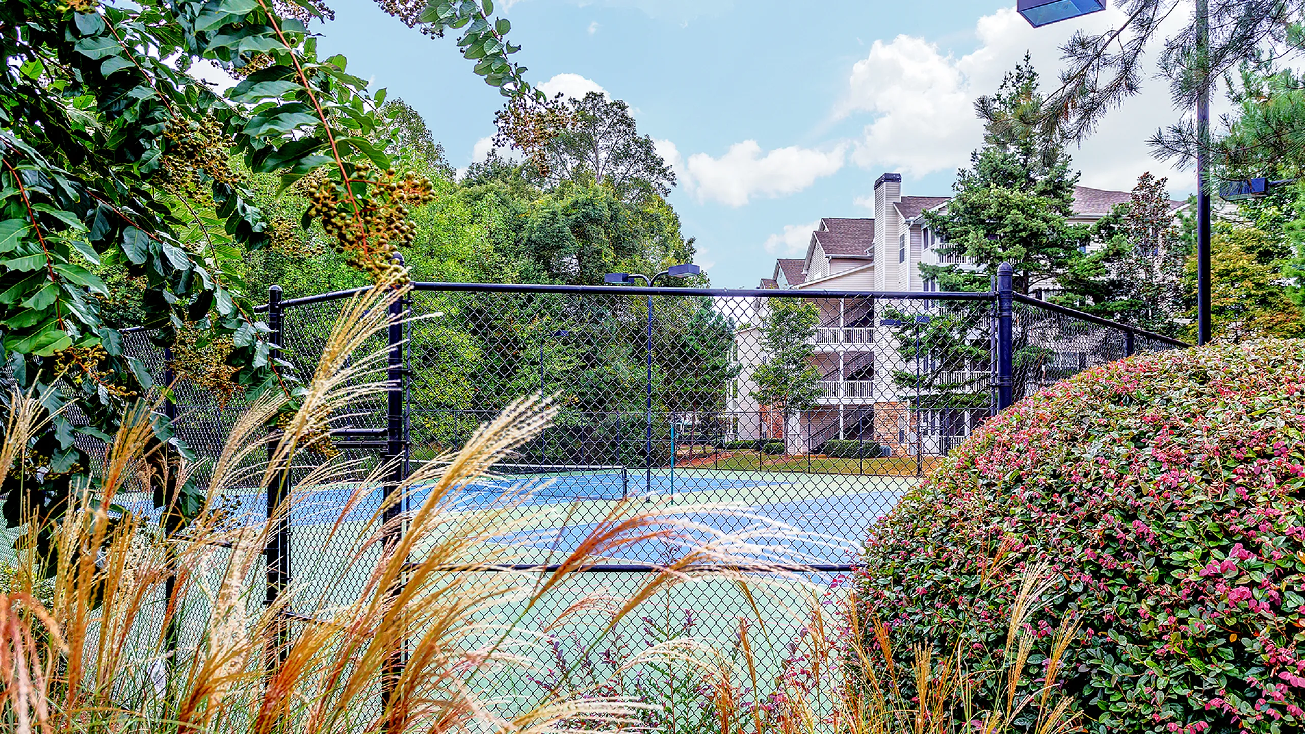 Charming community tennis court surrounded by lush greenery and vibrant flowers, with elegant apartments in the background at Summer Park Apartments in Buford GA
