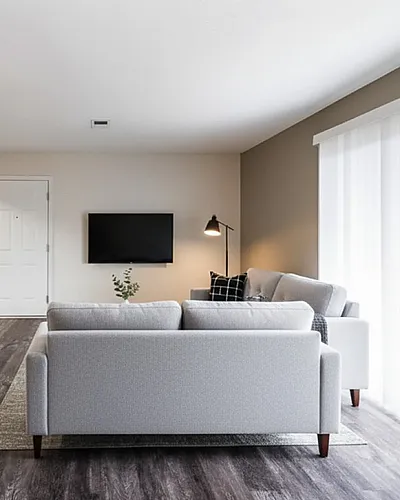 Bright and modern living room with elegant gray sofas, sleek hardwood floors, and a stylish open kitchen area.