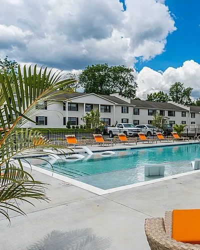 Stylish apartment complex featuring a sparkling outdoor pool with vibrant orange loungers and umbrellas, surrounded by lush greenery and modern amenities.