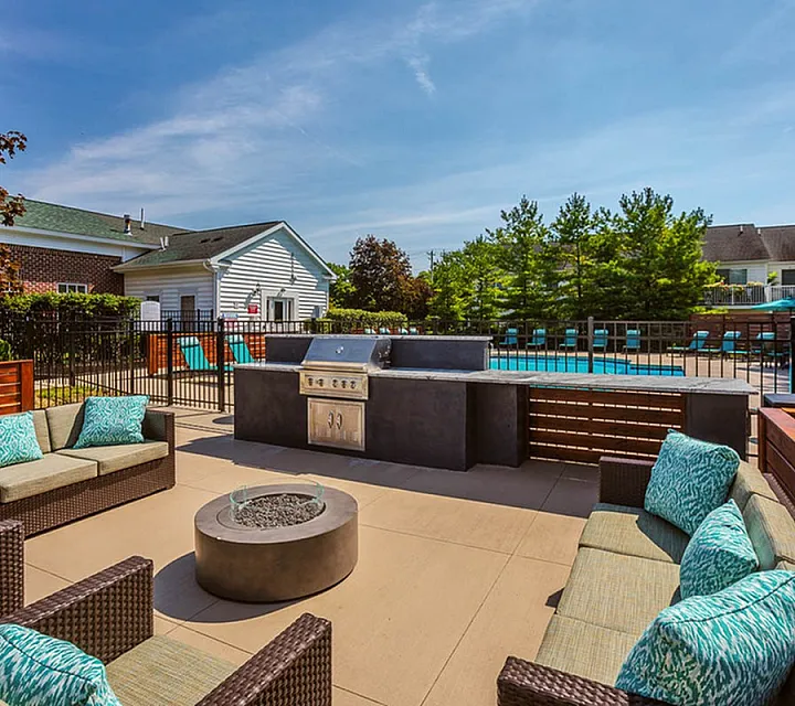 Inviting outdoor patio with modern seating, a sleek barbecue grill, and a sparkling pool surrounded by lush greenery, perfect for entertaining.