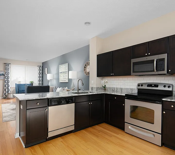 Modern open-plan kitchen with stainless steel appliances, elegant countertops, and a cozy living area, featuring stylish decor and warm wood flooring.