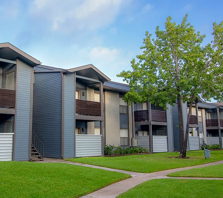Charming apartment complex with private balconies, nestled in a serene green landscape and clear blue skies.