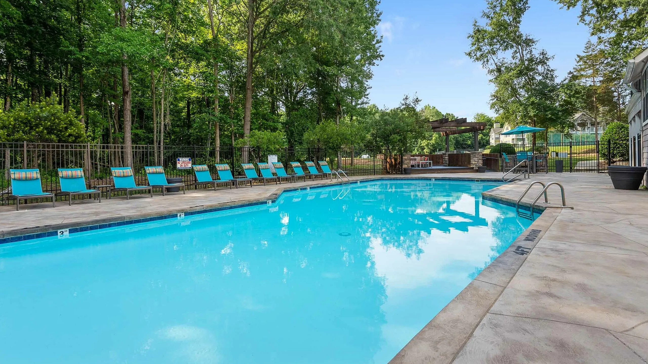 Inviting outdoor pool area surrounded by lush trees and stylish lounge chairs, perfect for relaxation and leisure.