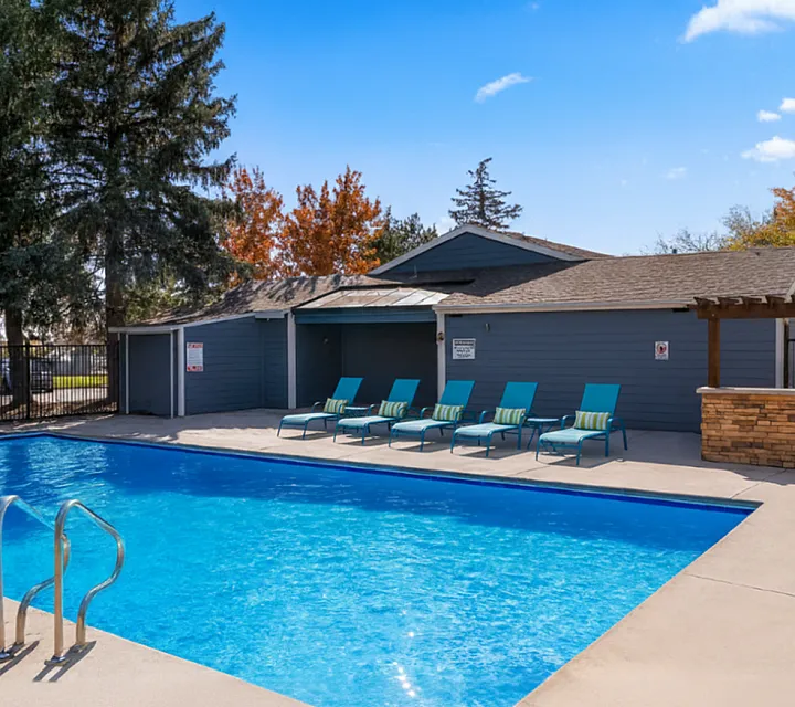 Inviting outdoor pool area with sleek loungers surrounded by vibrant autumn trees, perfect for relaxation and leisure.
