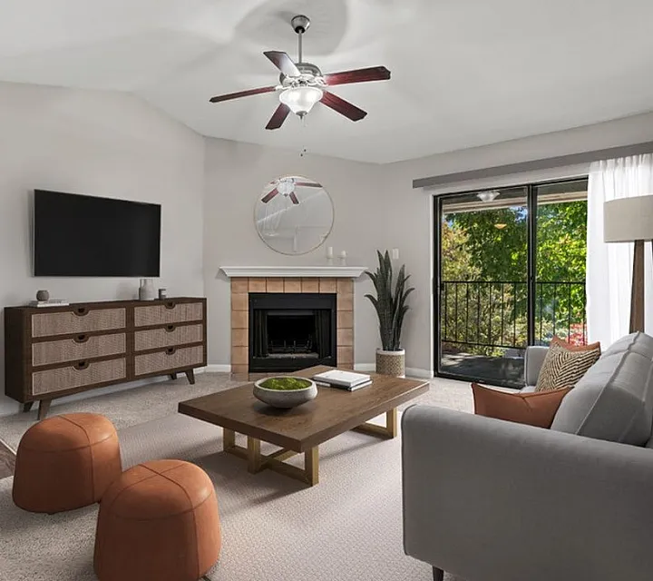 Bright and inviting living room featuring a modern design with a cozy fireplace, sleek ceiling fan, and large glass doors opening to lush greenery.
