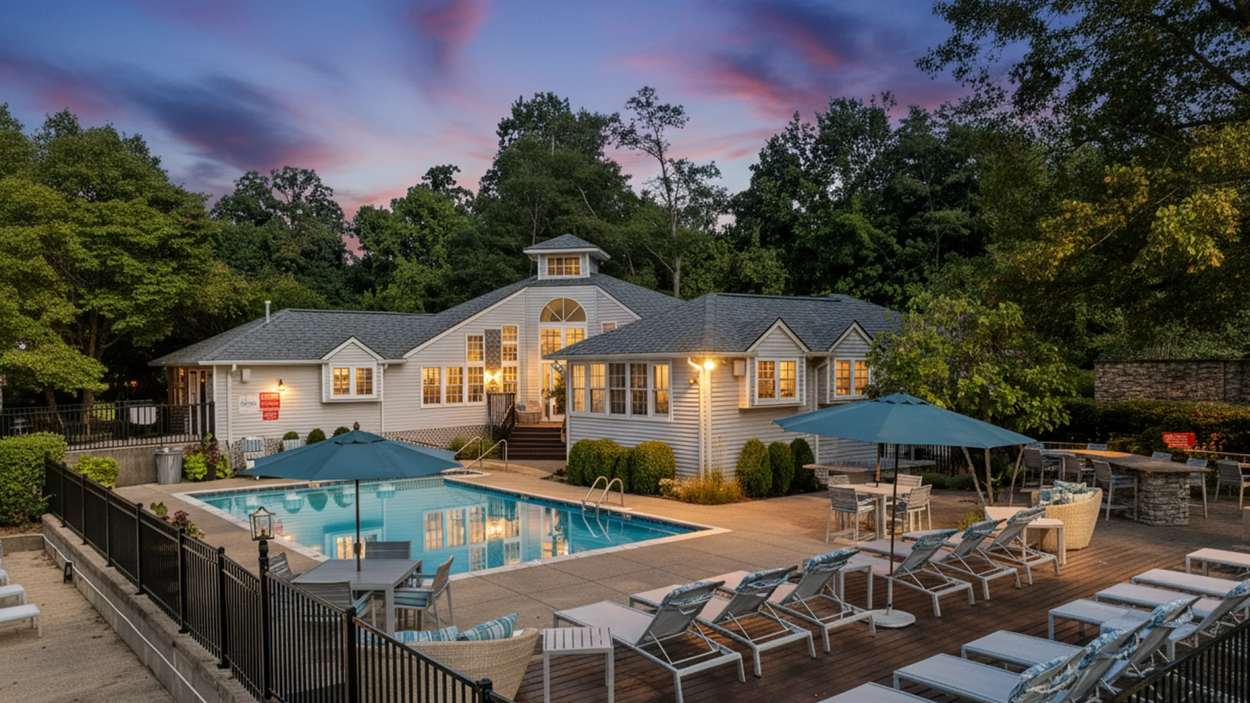 Charming residential complex with inviting poolside ambiance, surrounded by lush greenery and elegant lounge chairs at sunset.