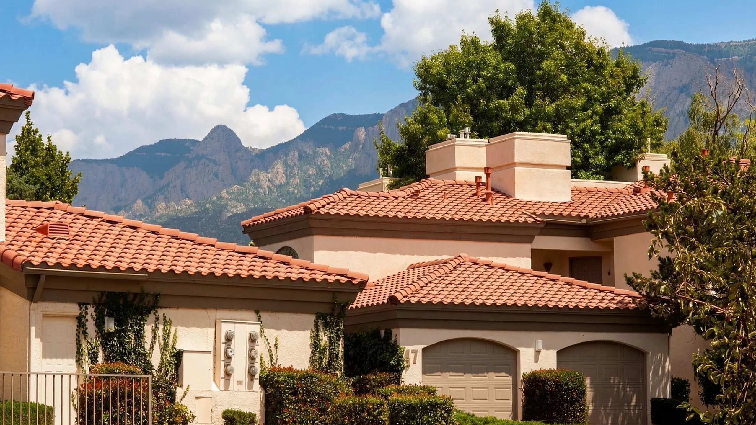 Charming villa with terracotta roof nestled in lush greenery, featuring stunning mountain views under a bright blue sky at Pavilions Apartments