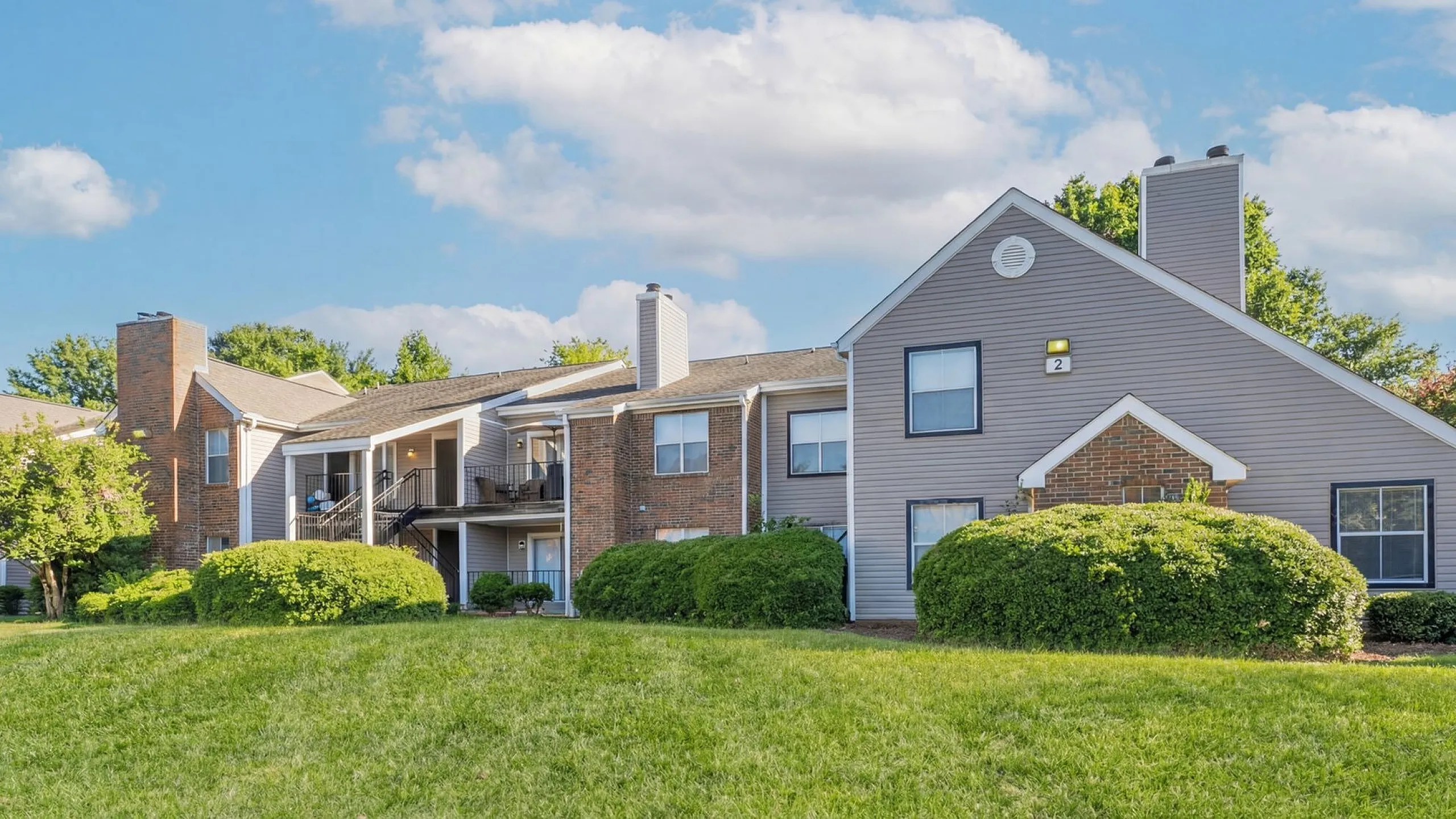 Charming apartment complex with a mix of brick and siding exteriors, nestled among lush greenery and under a clear blue sky at Park at Midtown Apartments