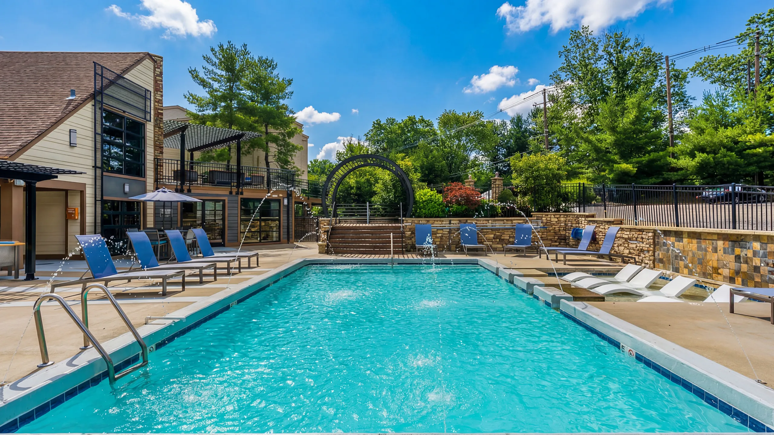 Inviting outdoor pool area with elegant lounge chairs and vibrant landscaping, perfect for relaxation under the clear blue sky at Creeks at Kirklevington Apartments in Lexington KY