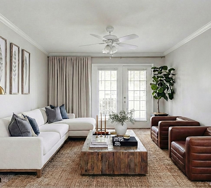 Inviting modern living room with a chic white sofa, cozy leather armchairs, elegant decor, and warm natural light flowing through large French doors at Stratford at Hillcrest Apartments in Winston-Salem.