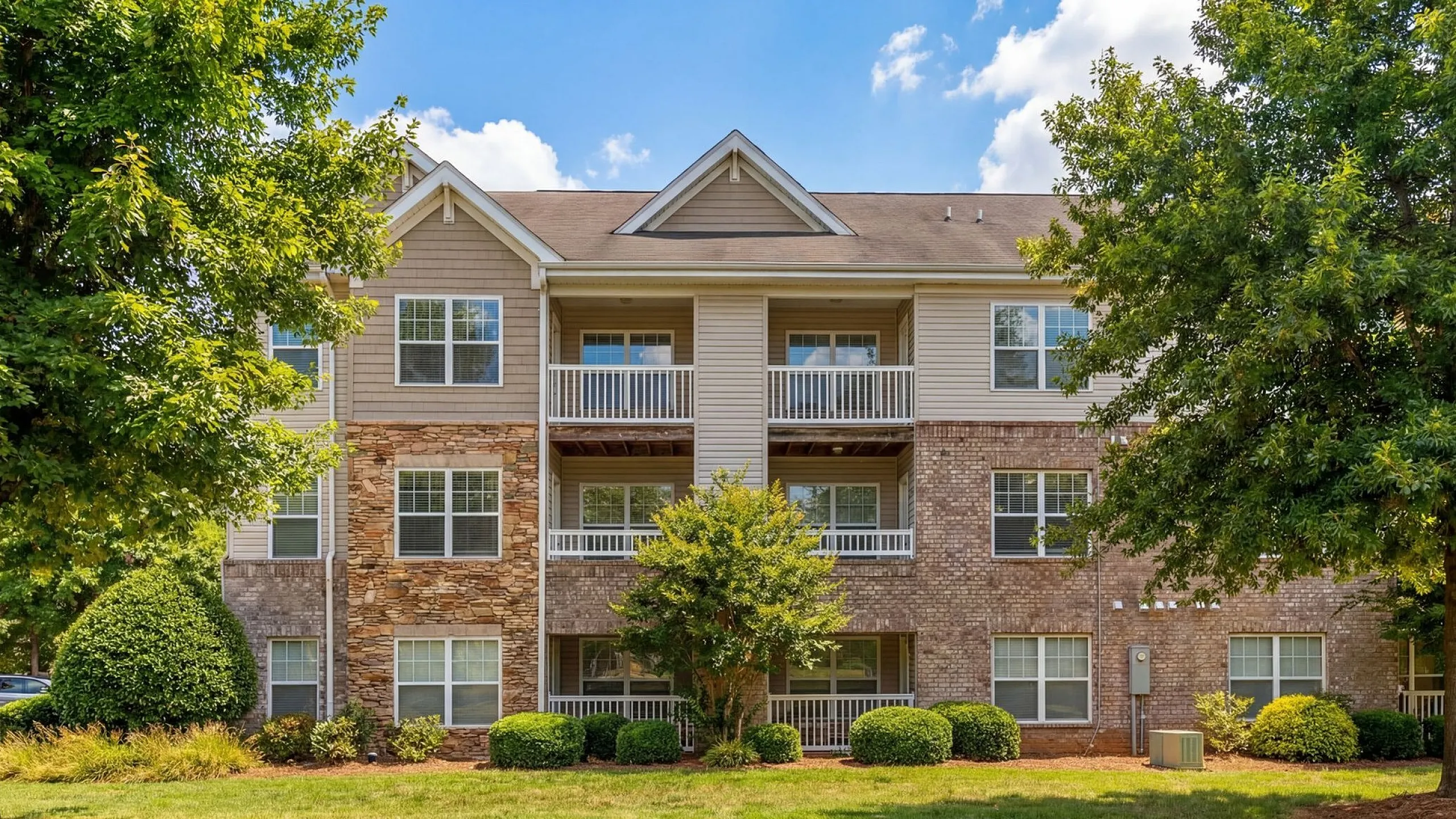 Charming apartment building with stylish brick and siding facade, surrounded by lush greenery and featuring inviting balconies at Stratford at Hillcrest Apartments in Winston-Salem.