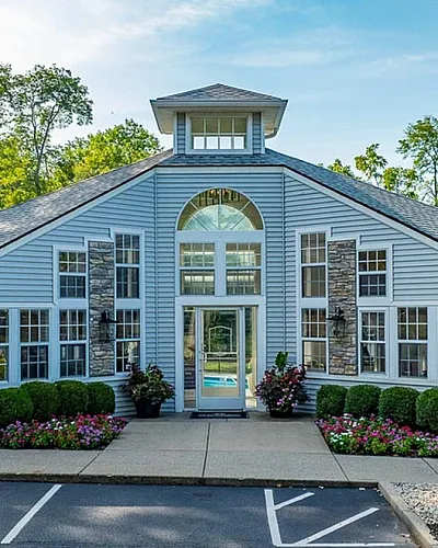 Charming leasing office with classic architecture surrounded by lush greenery and vibrant flowers, offering a warm welcome to The Retreat community at Retreat at Stillmeadow Apartments