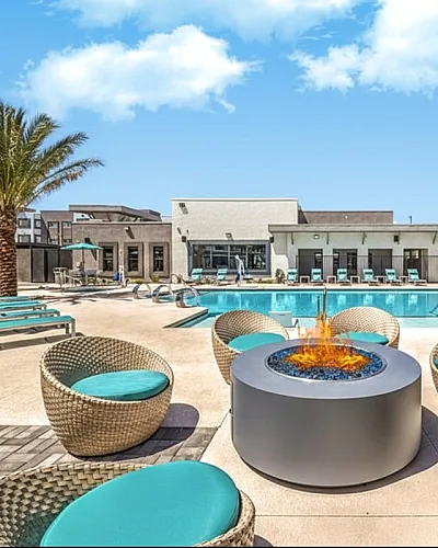 Luxurious resort-style apartment pool area with inviting lounge chairs, modern fire pit, and palm trees under a vibrant blue sky.