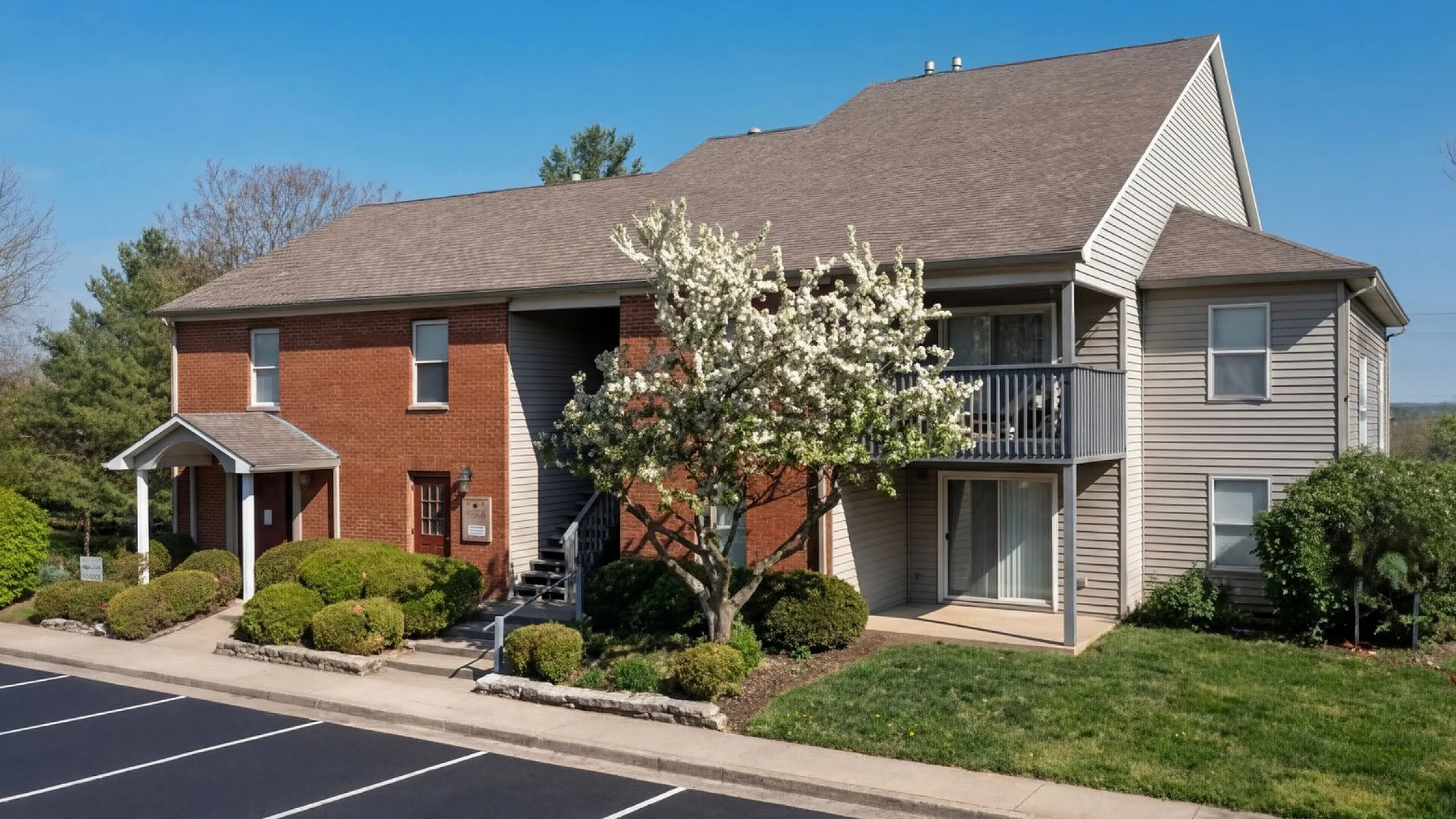 Charming apartment complex with elegant brick and siding exterior, beautifully landscaped greenery, and spacious balconies, offering serene living in a peaceful neighborhood at Crown Pointe Apartments