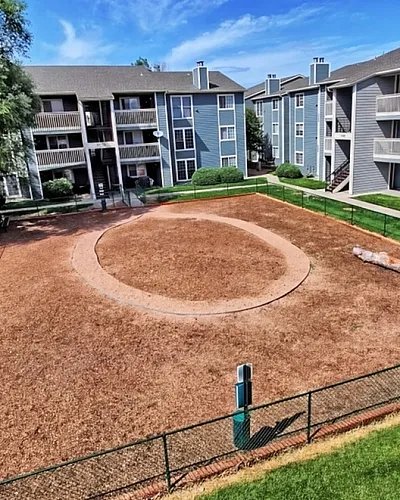 Charming apartment community with lush green lawns, spacious play area, and modern architecture under a clear blue sky.