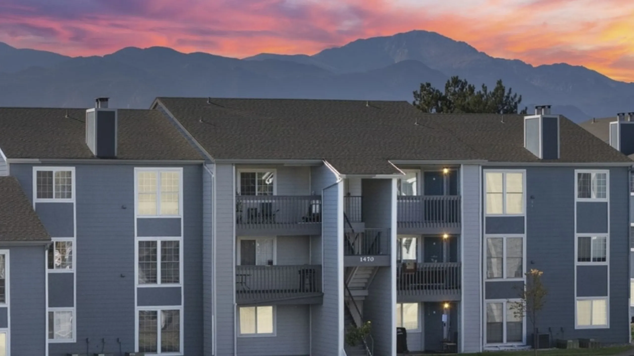 Charming apartment building set against a breathtaking sunset, featuring contemporary architecture and well-lit interiors.