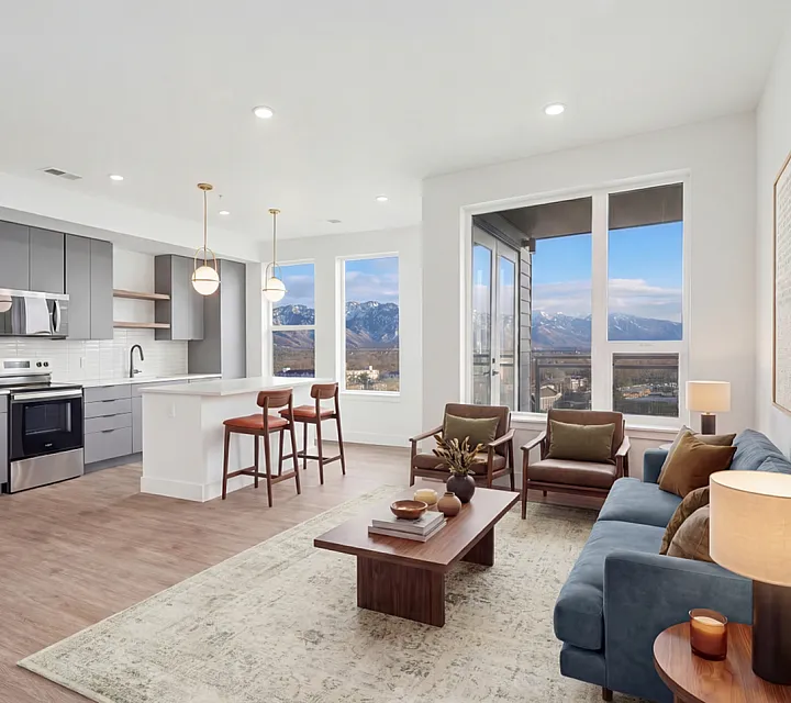 Modern open-plan living room and kitchen with stunning mountain views, featuring elegant furniture, a sleek kitchen island, and large windows inviting natural light at The Westerly in Millcreek Utah