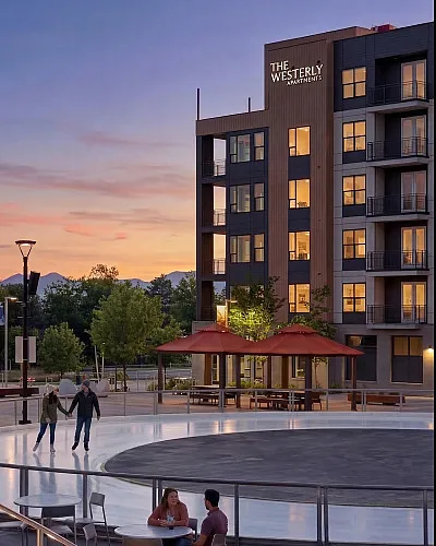 Charming sunset view of The Westerly Apartments with a vibrant social courtyard featuring couples skating and dining, surrounded by lush greenery.