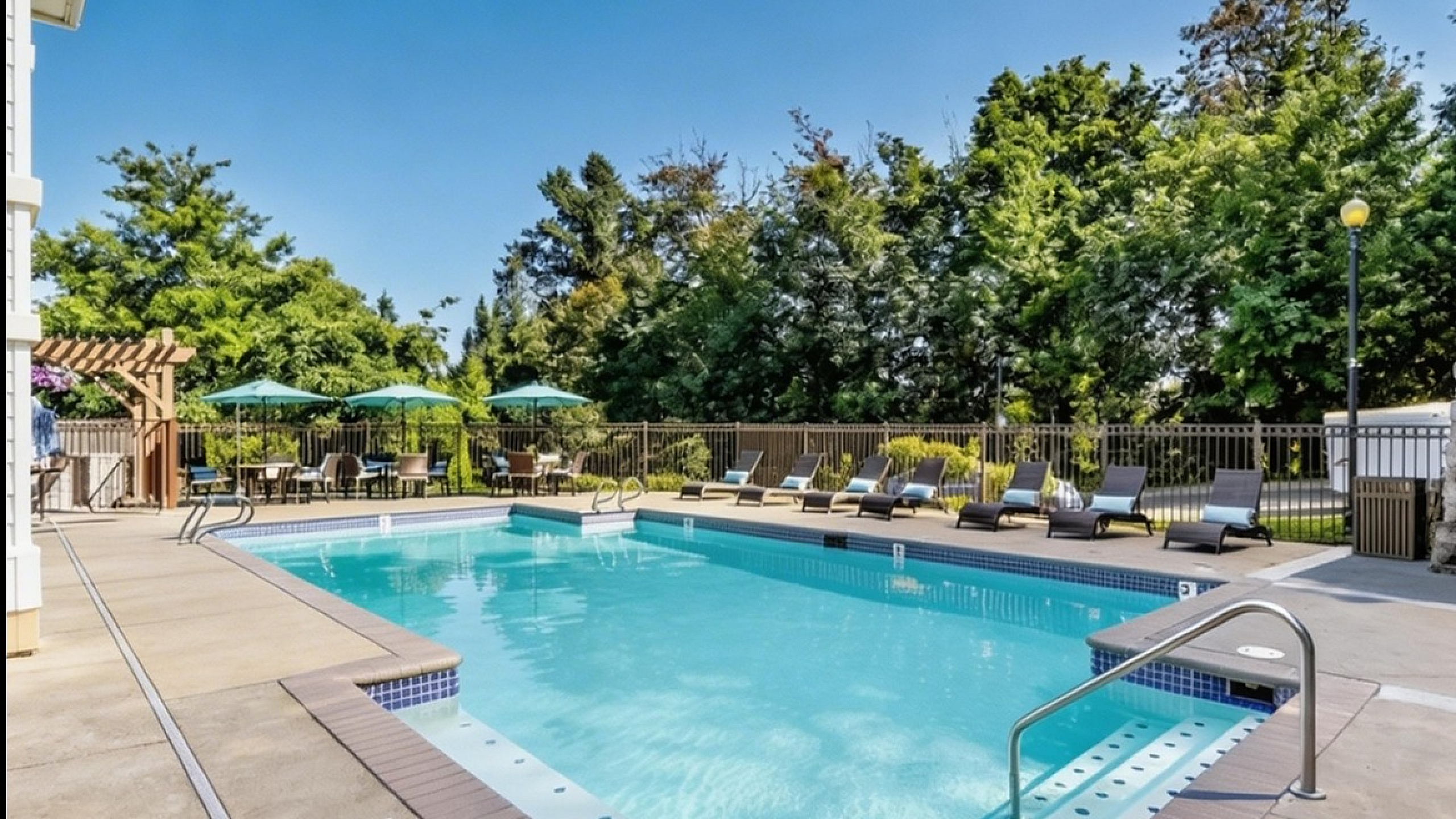 Inviting outdoor swimming pool area with comfortable lounge chairs, shaded seating, and lush green trees in the background, perfect for relaxation.