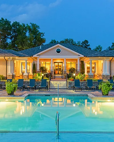 Luxurious apartment complex with inviting poolside view, elegant architecture, and lush landscaping at dusk.