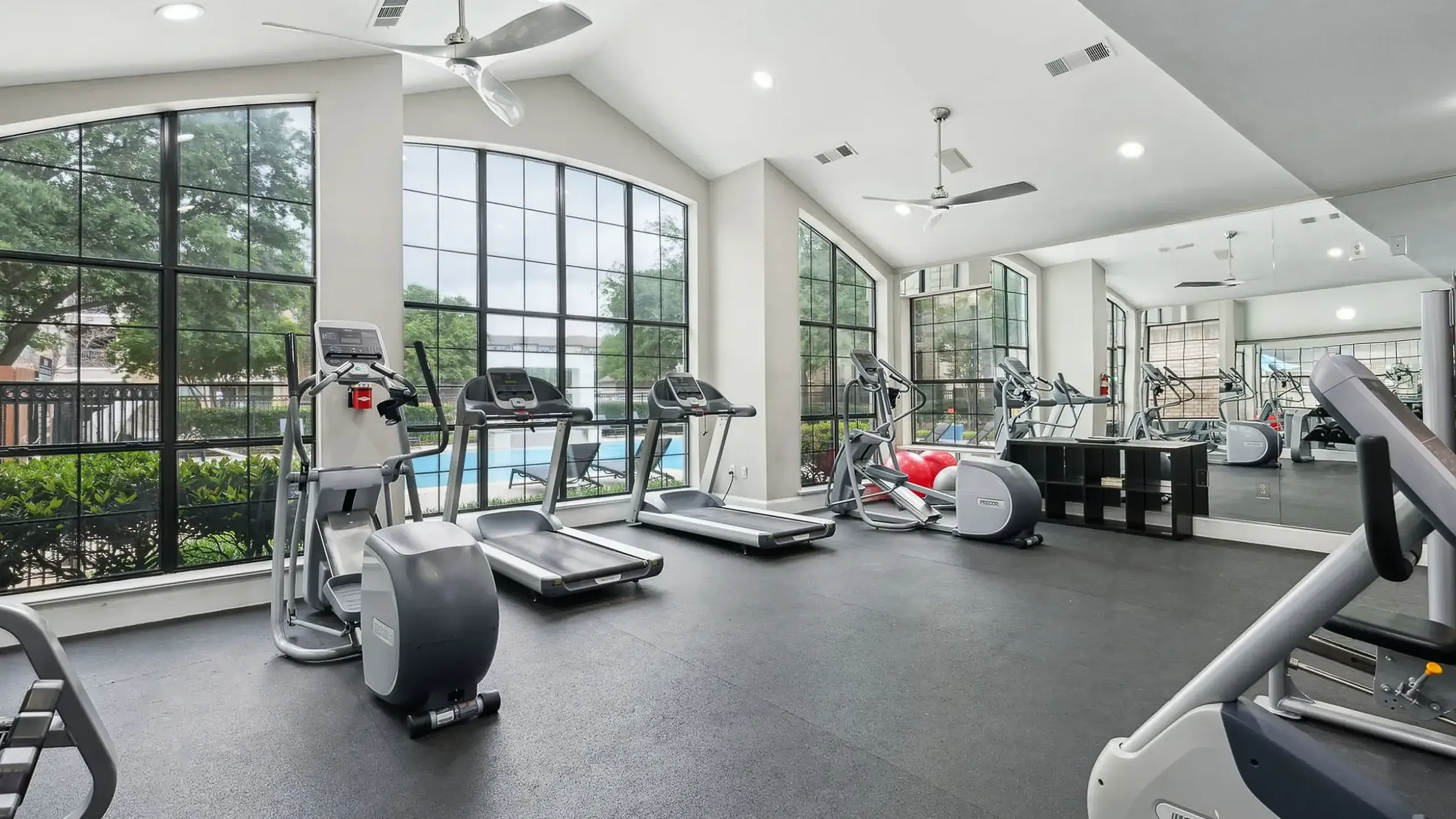 Elegant fitness center with modern equipment, large windows with pool view, and mirrored walls for a bright and open workout atmosphere.