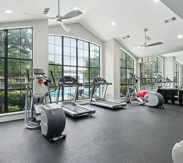 View of Modern fitness center with large windows, treadmills, exercise bikes, and a view of the pool.