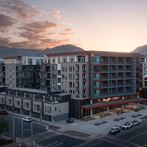 Modern apartment complex at sunset, framed by majestic mountains, showcasing sleek architecture and vibrant urban living.