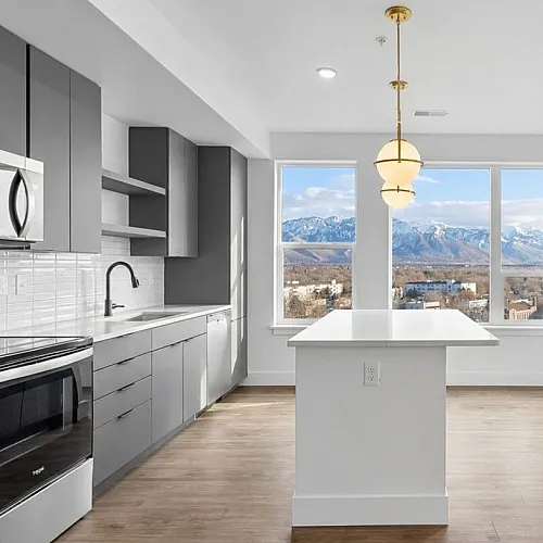 Contemporary kitchen with sleek gray cabinets, modern appliances, and expansive mountain views through large windows, featuring elegant pendant lighting.