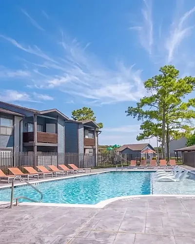 Charming apartment complex with modern pool area surrounded by elegant lounging chairs, accentuated by a serene sunset backdrop.