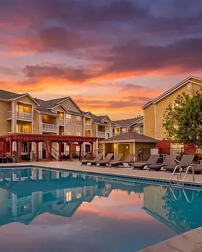 Charming sunset view of a lovely apartment complex, The Orchards at Cherry Creek Park, featuring serene poolside relaxation and elegant lounging chairs.
