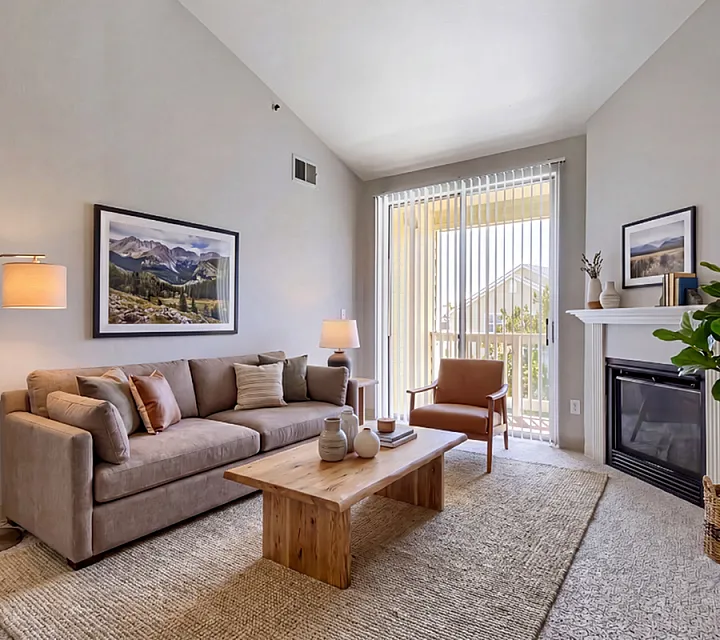 Bright and inviting living room featuring a cozy beige couch, wooden coffee table, and elegant fireplace with natural light streaming through large windows.