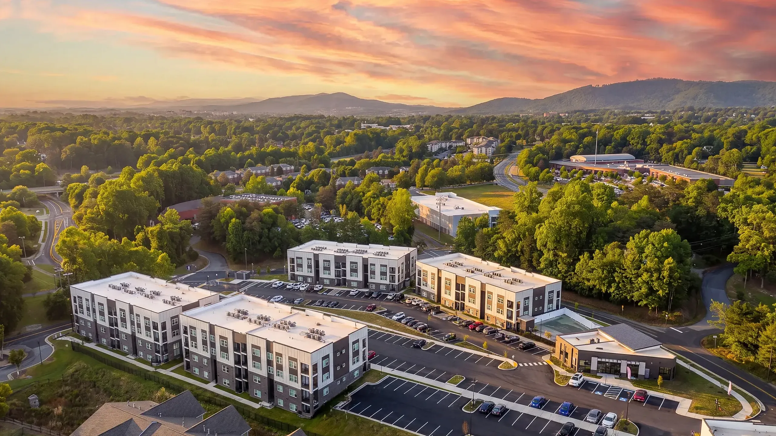 Scenic aerial view of modern apartment complex surrounded by lush greenery and vibrant skies, offering a serene living environment.