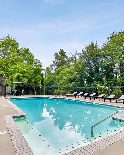 Inviting outdoor pool area with sleek lounge chairs, surrounded by lush greenery and a modern building backdrop, ideal for relaxation and summer enjoyment.