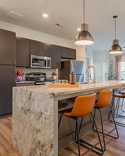 Bright and modern open-concept living space featuring a sleek kitchen with dark cabinetry, stylish dining area, and cozy living room with abundant natural light.