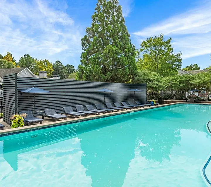 Inviting outdoor pool area with modern lounge chairs and vibrant landscaping under a clear blue sky.