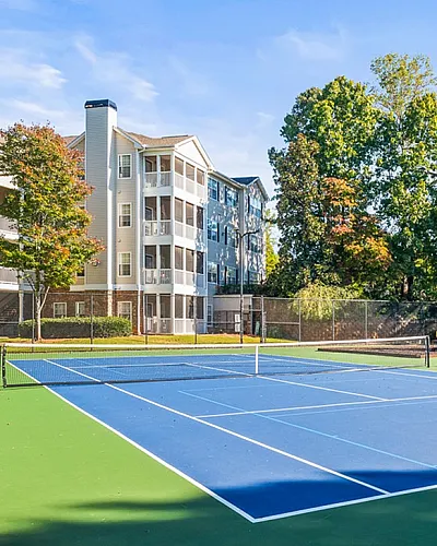 Vibrant apartment community featuring a tennis court and colorful playground, surrounded by lush greenery and elegant buildings.