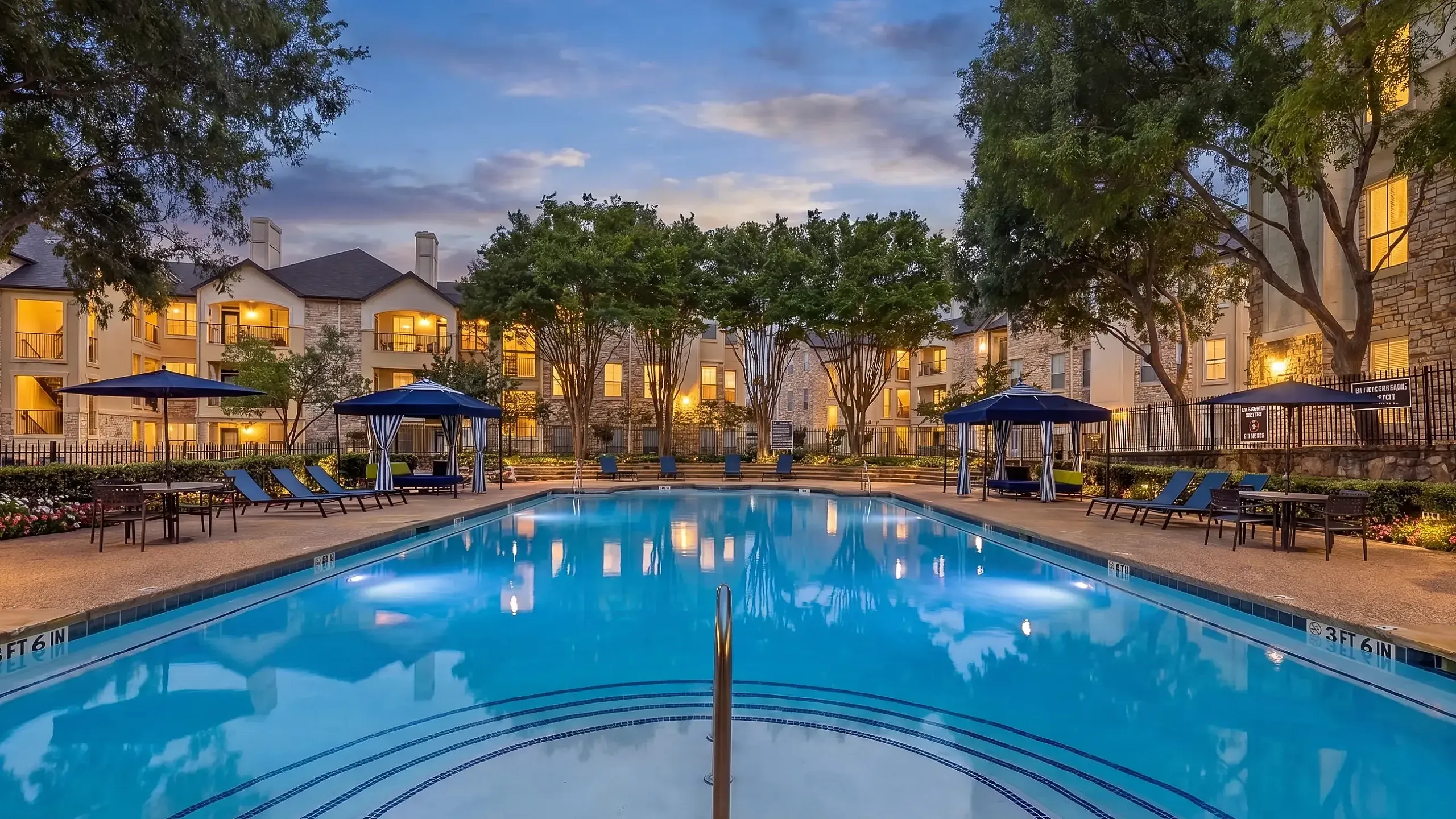 Luxurious poolside view at a modern apartment complex, featuring tranquil waters, green cabanas, and lush landscaping under a bright blue sky at Stonebriar at Frisco Apartments