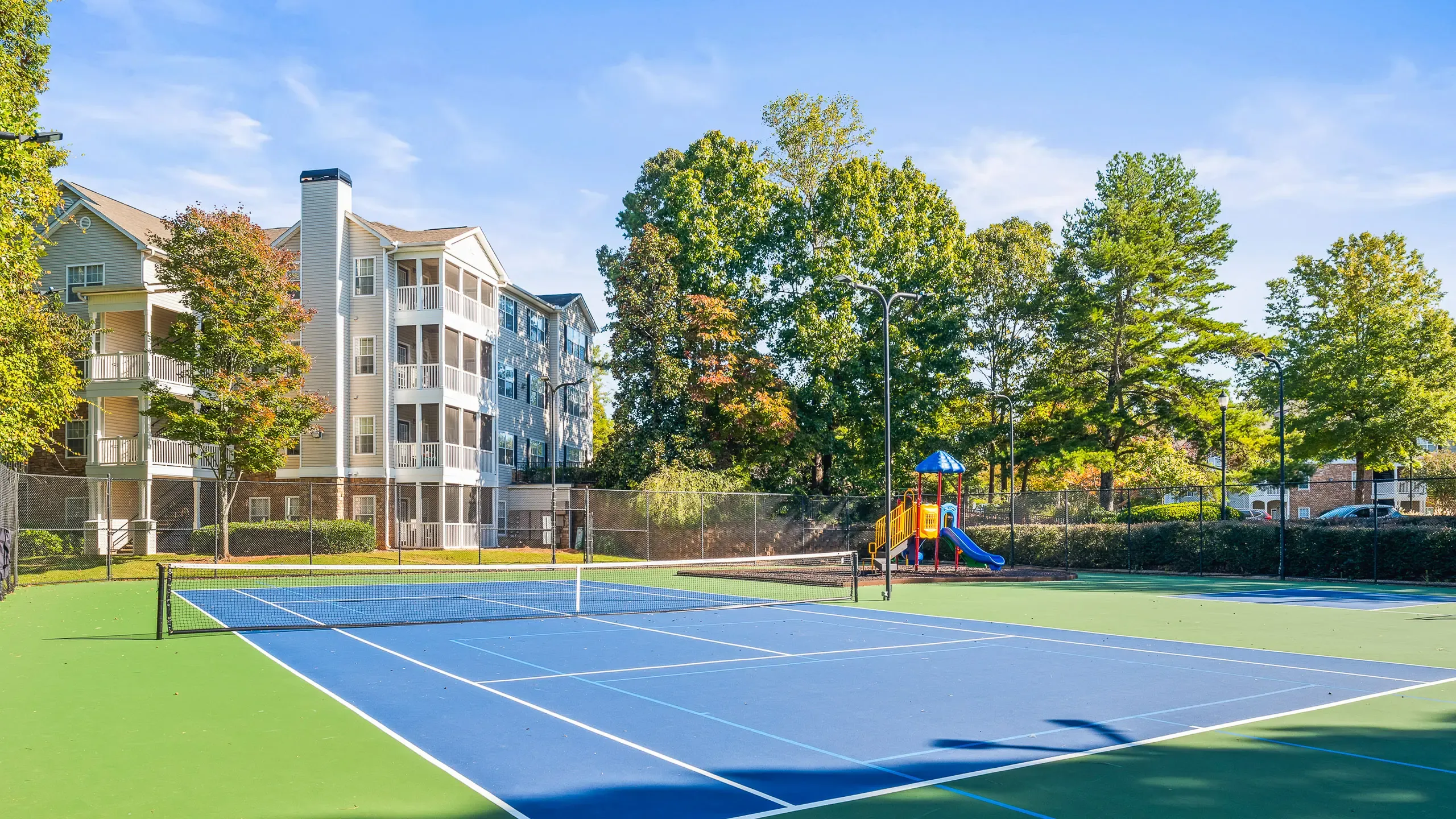 Inviting apartment complex, Summer Park, with picturesque tennis court and vibrant playground, surrounded by lush greenery.