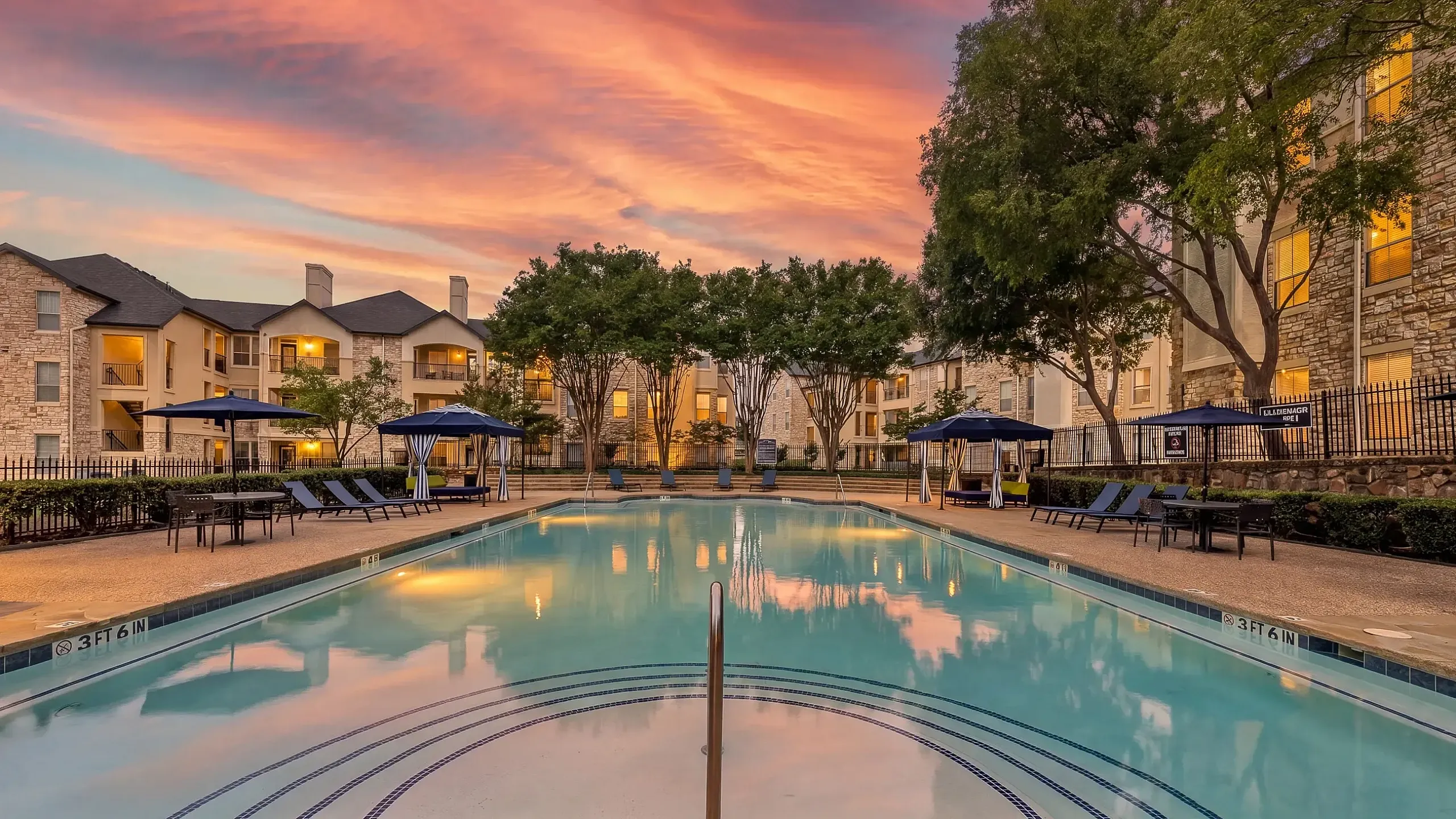 Luxurious poolside view at a modern apartment complex, featuring tranquil waters, green cabanas, and lush landscaping under a bright blue sky at Stonebriar at Frisco Apartments