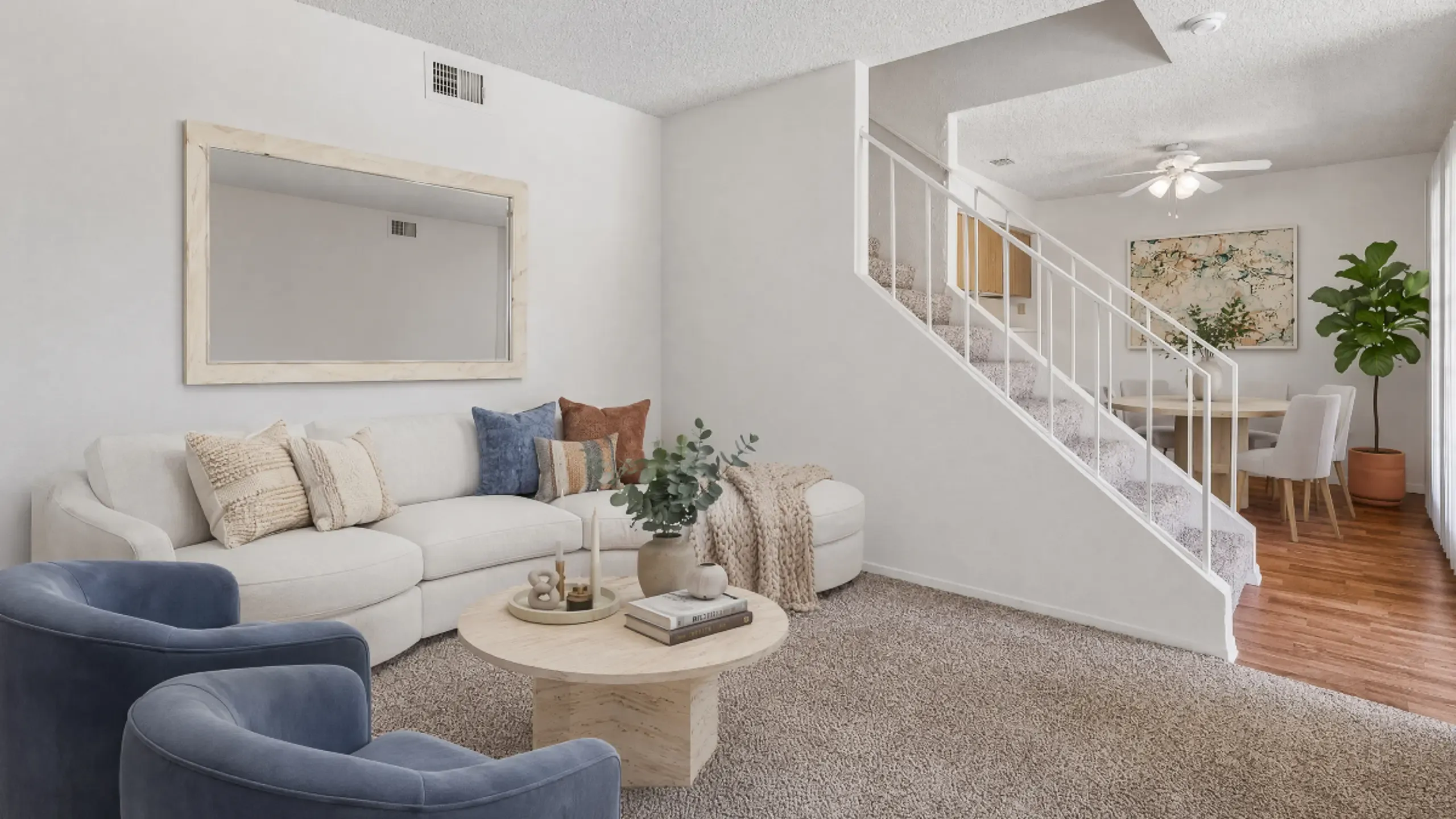 Inviting living room with cozy beige sofa, stylish blue chairs, and elegant decor, leading to a dining area with modern furniture and large artwork at Camelot Apartments in Yuma, AZ.